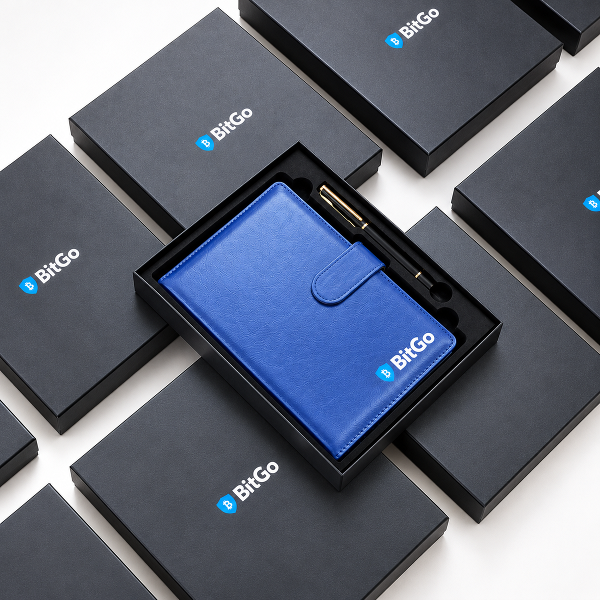Open black gift box containing a blue BitGo notebook and black pen with gold-coloured trim, surrounded by closed BitGo-branded boxes