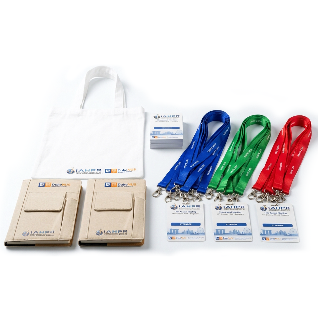 White tote bag and beige pocket notebooks with IAHPR and Duke-NUS logos, alongside blue, green and red lanyards with attendee badges