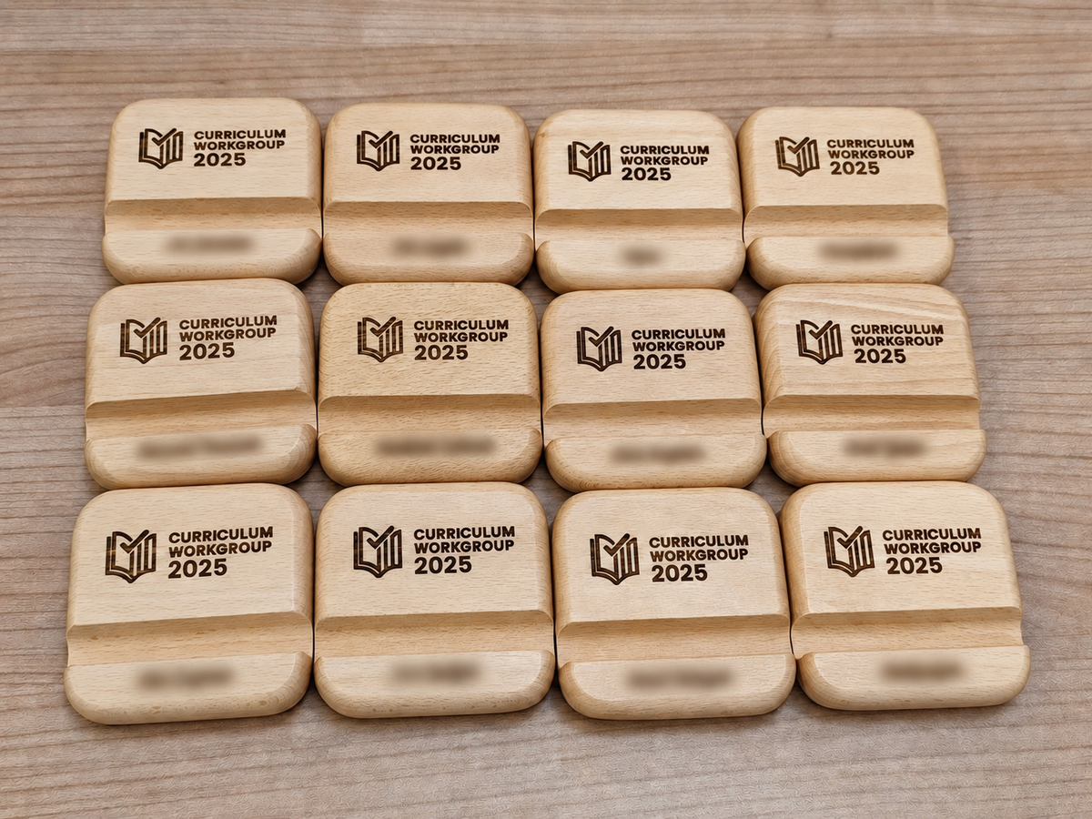 Wooden phone stands with rounded corners engraved with Curriculum Workgroup 2025 branding