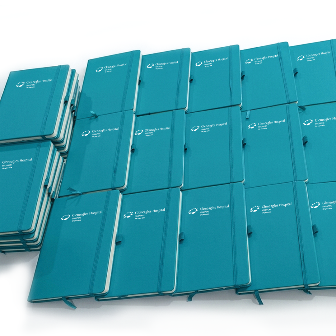 Cyan notebooks with matching elastic straps and white Gleneagles Hospital branding, arranged in rows and stacks on a white background