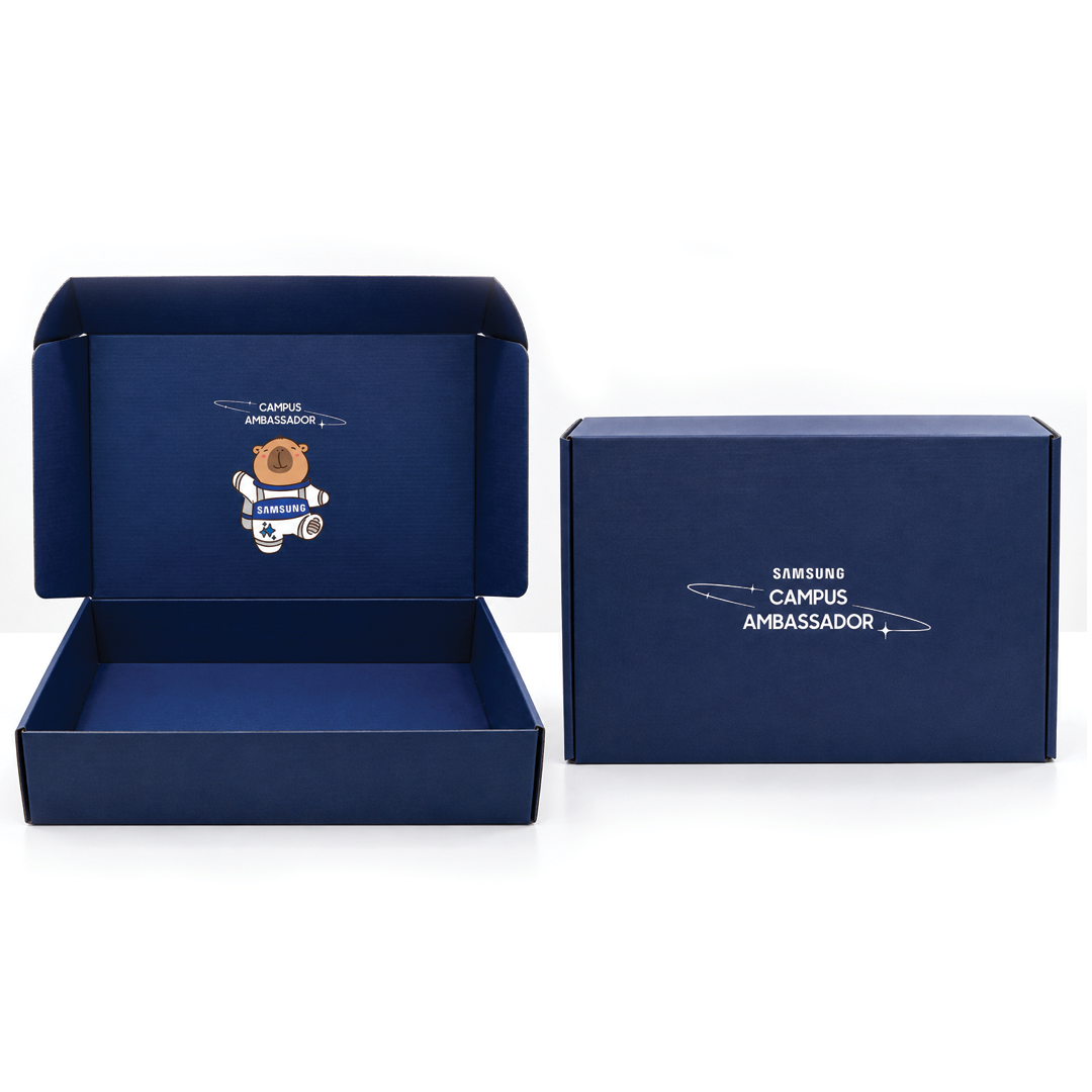 Two navy blue Samsung Campus Ambassador gift boxes side by side, one open showing astronaut mascot artwork inside the lid and one closed showing white branding